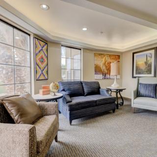 A cozy living room with comfortable seating and large windows, adorned with artwork.