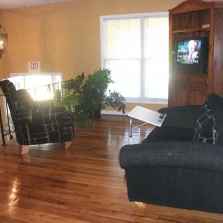 A cozy living room with a sofa, armchair, and entertainment center featuring a television, set against hardwood floors and a large window.