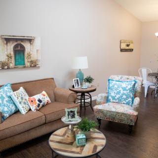 A cozy living room with a brown sofa, patterned armchair, and decorative pillows, featuring wall art and a wooden coffee table.