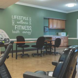 A fitness center room with green walls, motivational wall art, office chairs, and exercise equipment.