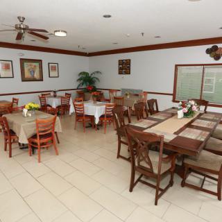 An empty dining room featuring several tables and chairs, decorated with plants and artwork on the walls.