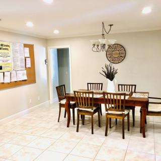 A cozy dining room with a wooden table and chairs, enhanced by a decorative wall piece and a notice board.