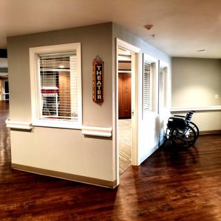 A well-lit hallway in a nursing home with a wheelchair parked beside a room entrance.