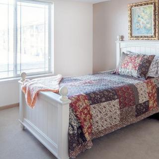 A cozy bedroom with a single bed adorned with a patchwork quilt, positioned near a large window that lets in natural light.