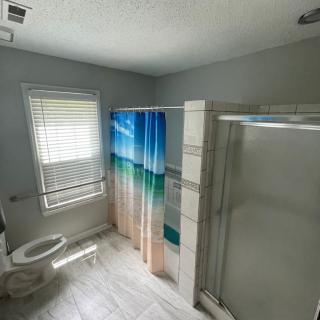 A bright and modern bathroom featuring a shower with a colorful curtain, a toilet, and a window with blinds.