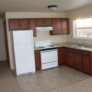A simple kitchen layout featuring wooden cabinets, a white refrigerator, stove, and a sink under the window.