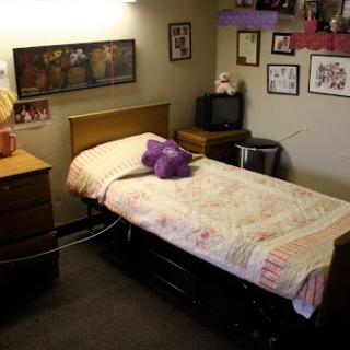 A cozy bedroom featuring a single bed with a purple stuffed animal, surrounded by personal touches and decor.