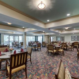 Elegant dining room with neatly arranged tables and chairs, featuring warm lighting and patterned carpet.