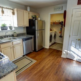 A cozy kitchen with wooden flooring and a connected laundry room.
