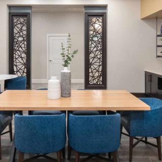 A modern dining area featuring a wooden table, blue chairs, and decorative vases, with ornamental wall panels in the background.