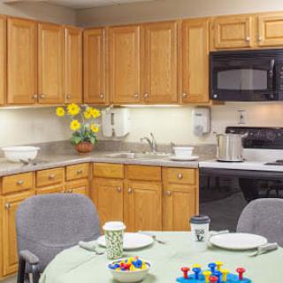 A cozy kitchen with wooden cabinets, a dining table set for a meal, and bright flowers on the counter.