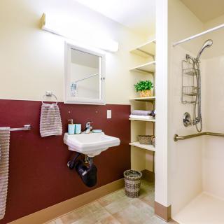 A well-lit bathroom with a sink, shower, and shelving.
