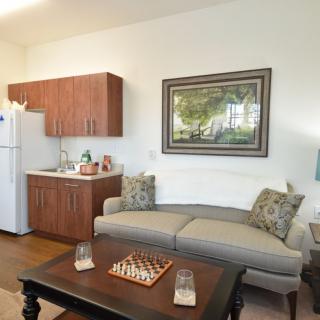 A cozy living area with a kitchenette, featuring a sofa and a chessboard on the coffee table.
