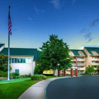 A welcoming hotel exterior at dusk, featuring well-maintained landscaping and an American flag.