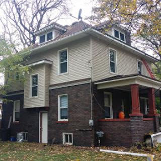 A two-story house featuring a mix of brick and siding, surrounded by autumn foliage.