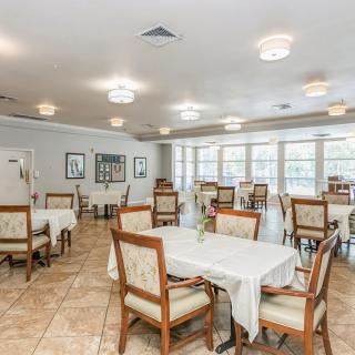 A spacious dining area with neatly arranged tables and chairs, well-lit by overhead lights and natural sunlight through large windows.