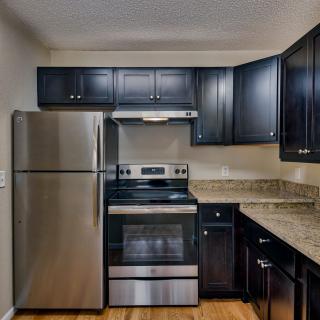 A modern kitchen featuring stainless steel appliances, black cabinets, and granite countertops.
