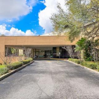 A building entrance with a driveway lined by trees under a partly cloudy sky.