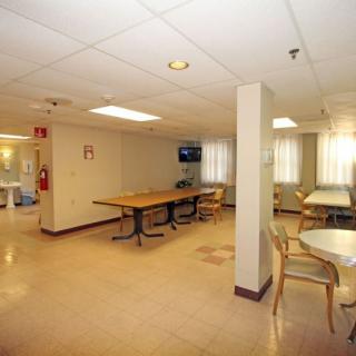 A spacious common area with tables, chairs, and a television, illuminated by bright lighting.