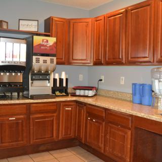 A kitchen area with wooden cabinets, a beverage dispenser, and blue water jugs on the countertop.