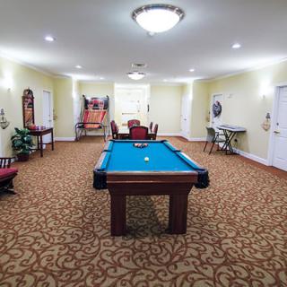A well-lit game room featuring a pool table and arcade game, set on a carpeted floor.