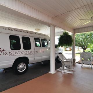 A transport van parked under a covered area with seating and potted plants nearby.
