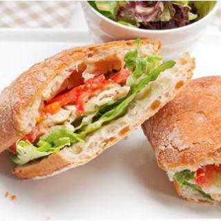 A delicious sandwich with chicken, lettuce, and vegetables served with a side salad.
