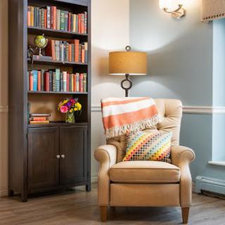 A cozy reading nook with an armchair, a lamp, and a bookshelf filled with books.