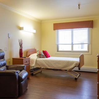 A hospital room with a single bed, a comfortable chair, and a window letting in natural light.