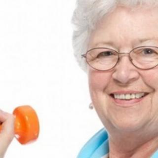 Elderly woman smiling while holding a dumbbell.
