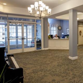 A well-lit lobby with a chandelier, featuring a reception desk and a piano.