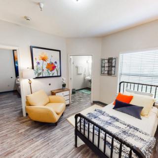 A modern bedroom interior with a bed, a comfortable chair, and colorful wall art.