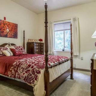 A cozy bedroom with a four-poster bed featuring red bedding, a window with curtains, and classic wooden furniture including a dresser and lamp.