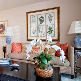 A cozy living room with a sofa adorned with decorative pillows, flanked by stylish lamps and complemented by wall art and a flower arrangement on the coffee table.
