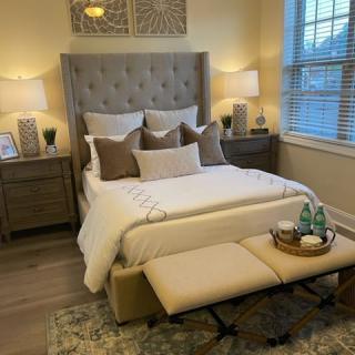 A beautifully decorated bedroom featuring a tufted bed with multiple pillows, bedside tables with lamps, and a bench at the foot of the bed.