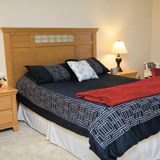 A cozy bedroom with a wooden bed frame, decorated with patterned bedding and a bedside lamp.