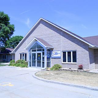 A modern single-story building with large windows and a sloped roof, set against a clear blue sky.