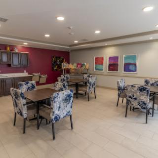 A modern dining area featuring floral-patterned chairs, a kitchen countertop, and colorful artwork on the walls.