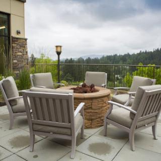 A cozy outdoor patio setup featuring comfortable chairs around a fire pit, with a scenic view of the surrounding landscape.