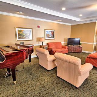 A cozy living room featuring a piano, comfortable seating, and a television.