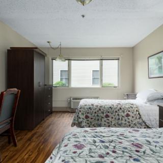 A cozy hotel room featuring two neatly made beds, large windows allowing natural light, and wooden flooring.