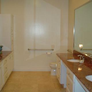 A spacious bathroom featuring a large mirror, double sinks, and a toilet.