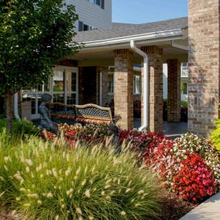 A charming garden area with a bench situated near a building entrance, surrounded by colorful flowers and lush greenery.