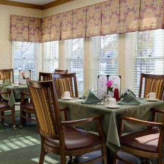 A cozy dining area with neatly arranged tables and chairs, illuminated by natural light from large windows.