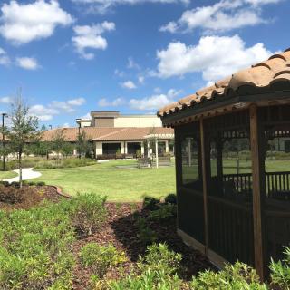 A sunny outdoor landscape featuring a gazebo in front of a large building.