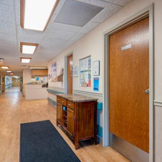 A well-lit hospital corridor featuring wooden doors and a reception area.