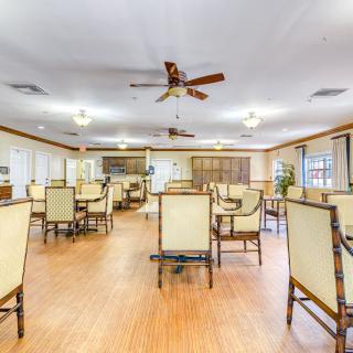 An empty dining room with neatly arranged tables and chairs, featuring ceiling fans and hardwood flooring.
