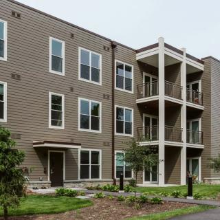 A modern three-story apartment building with balconies and landscaped surroundings.