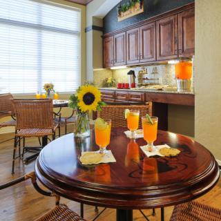 A cozy kitchen with a wooden table set for drinks, featuring sunflowers and wicker chairs.