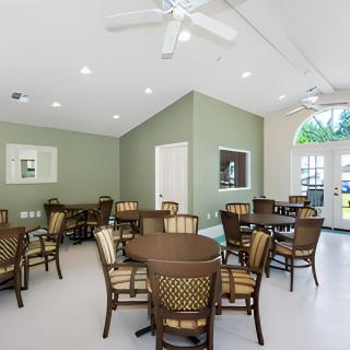 A cozy community dining area with multiple round tables and chairs, featuring green walls and a ceiling fan.